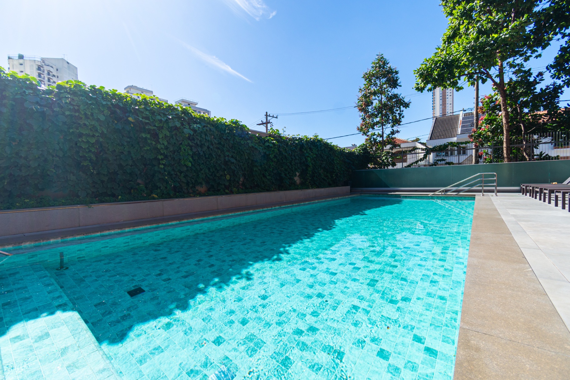 Piscina externa com deck de madeira e paredão verde